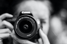 A black and white photo of a person holding a large professional camera up to the camera like they're taking a picture